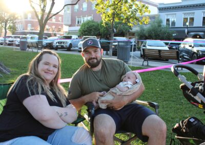 A man and woman sitting in chairs at a park with a baby