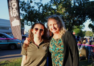 Two women hugging and smiling while at a bark with a tree and banner in the background