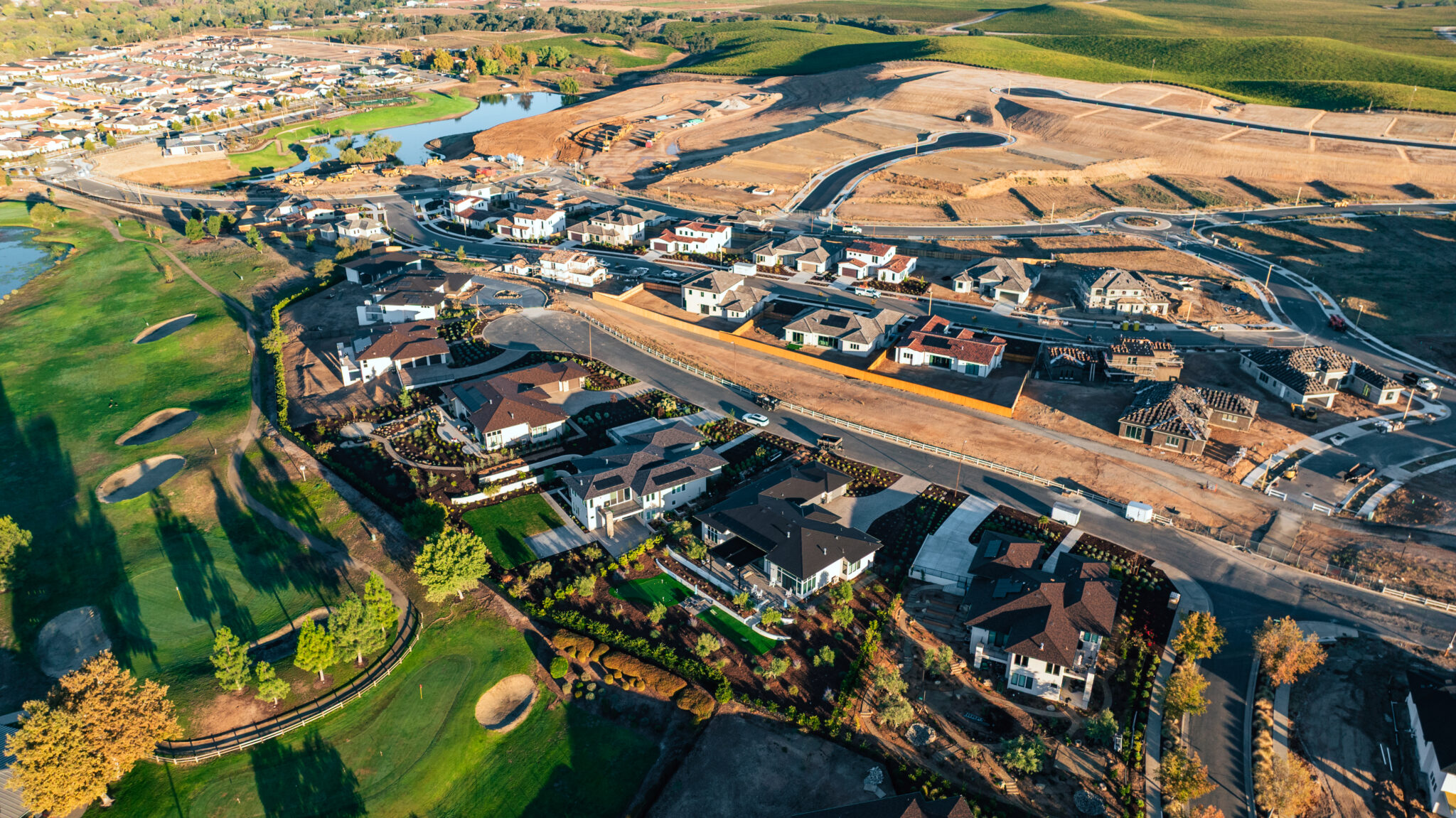  The Reserve at River Oaks shown from a bird's eye view, displaying a green golf course, rows of houses, and a field of undeveloped land