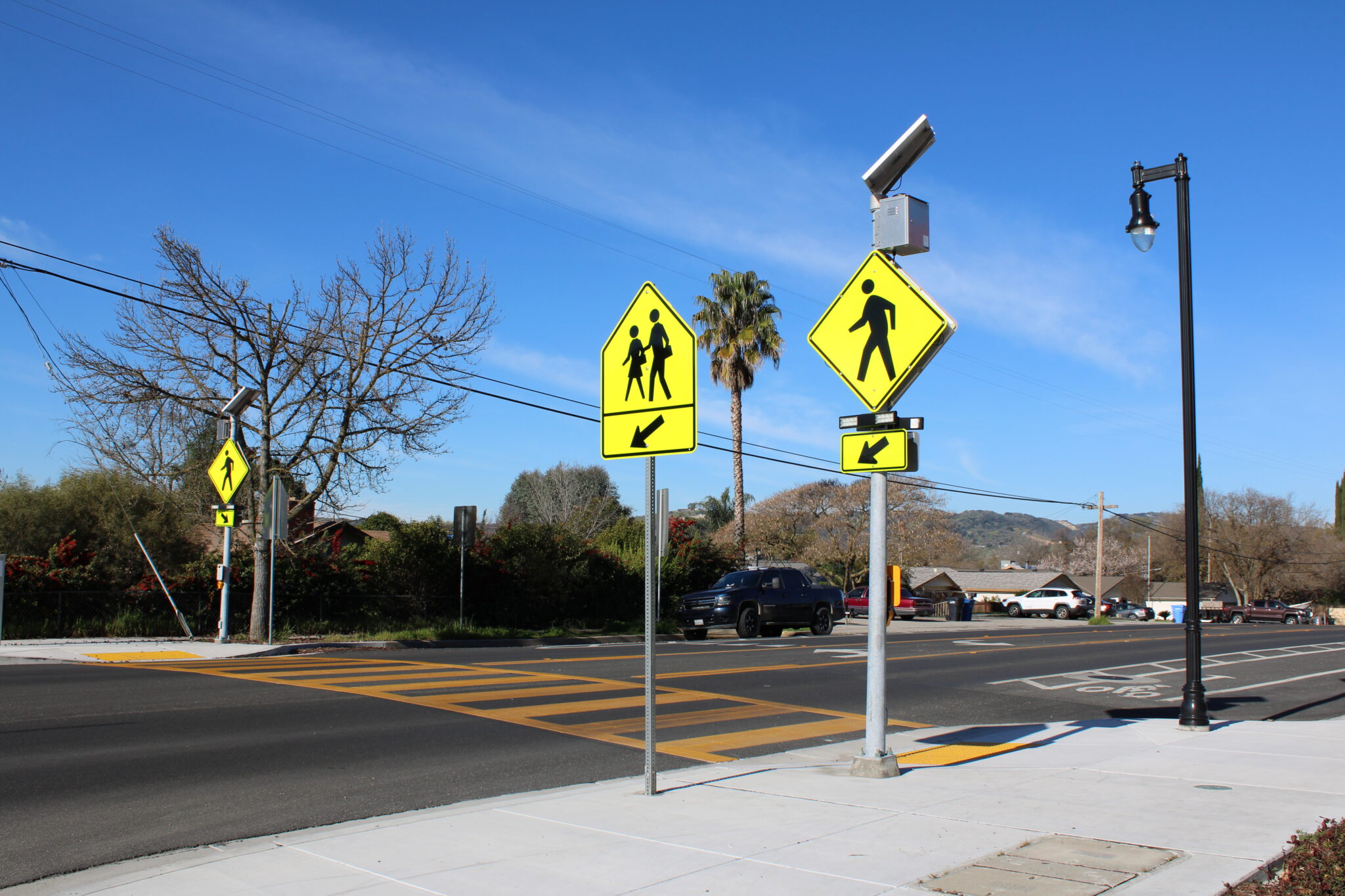 Street with orange crosswalk striping and neon green pedestrian crossing signs.