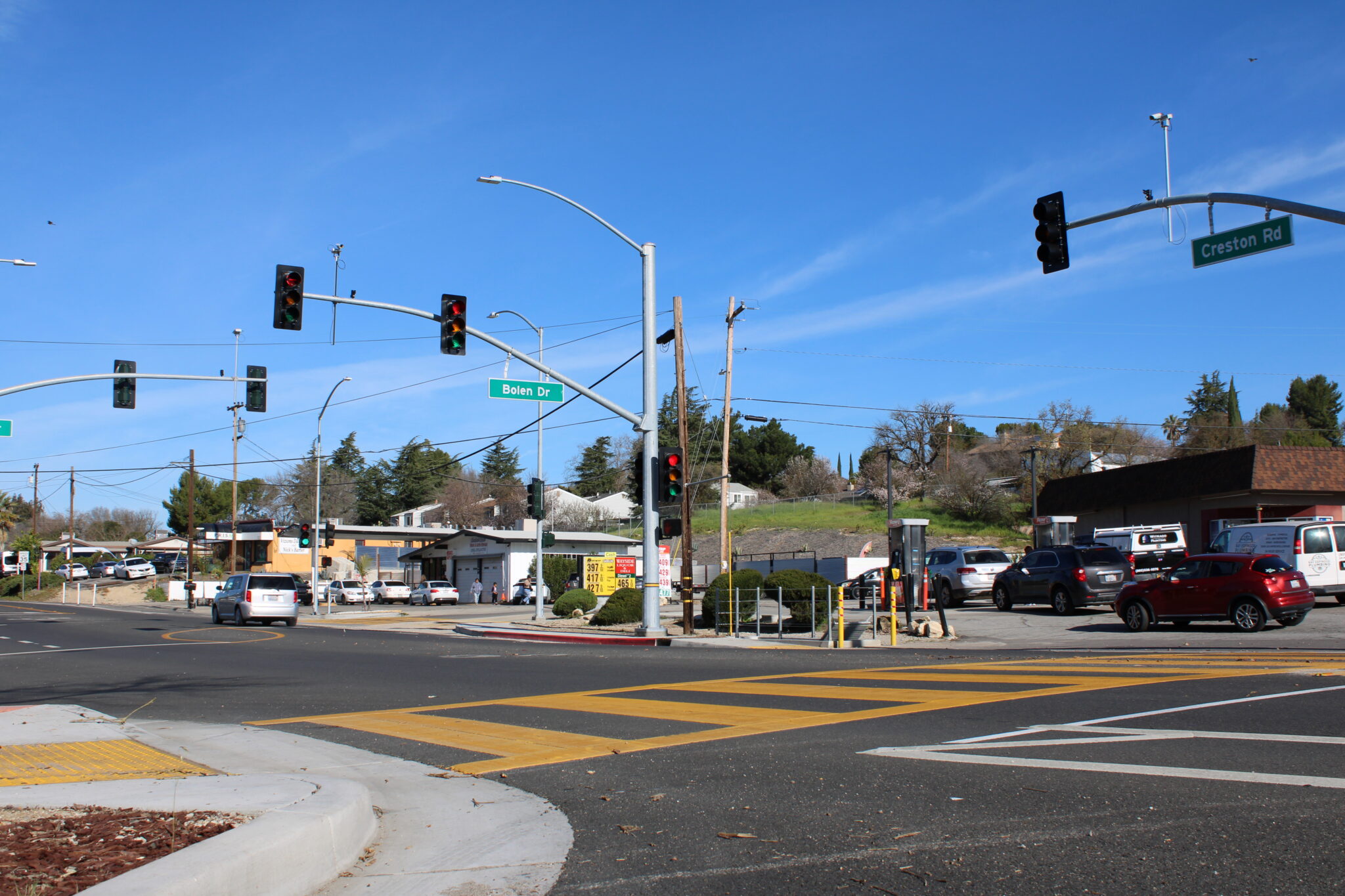 Intersection, newly paved road, and orange crosswalk striping with blue sky in the background